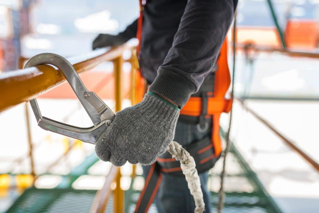 A close-up of a safety professional hooking a large metal carabiner onto a safety rail, demonstrating fall protection equipment used in Melbourne working at heights training.