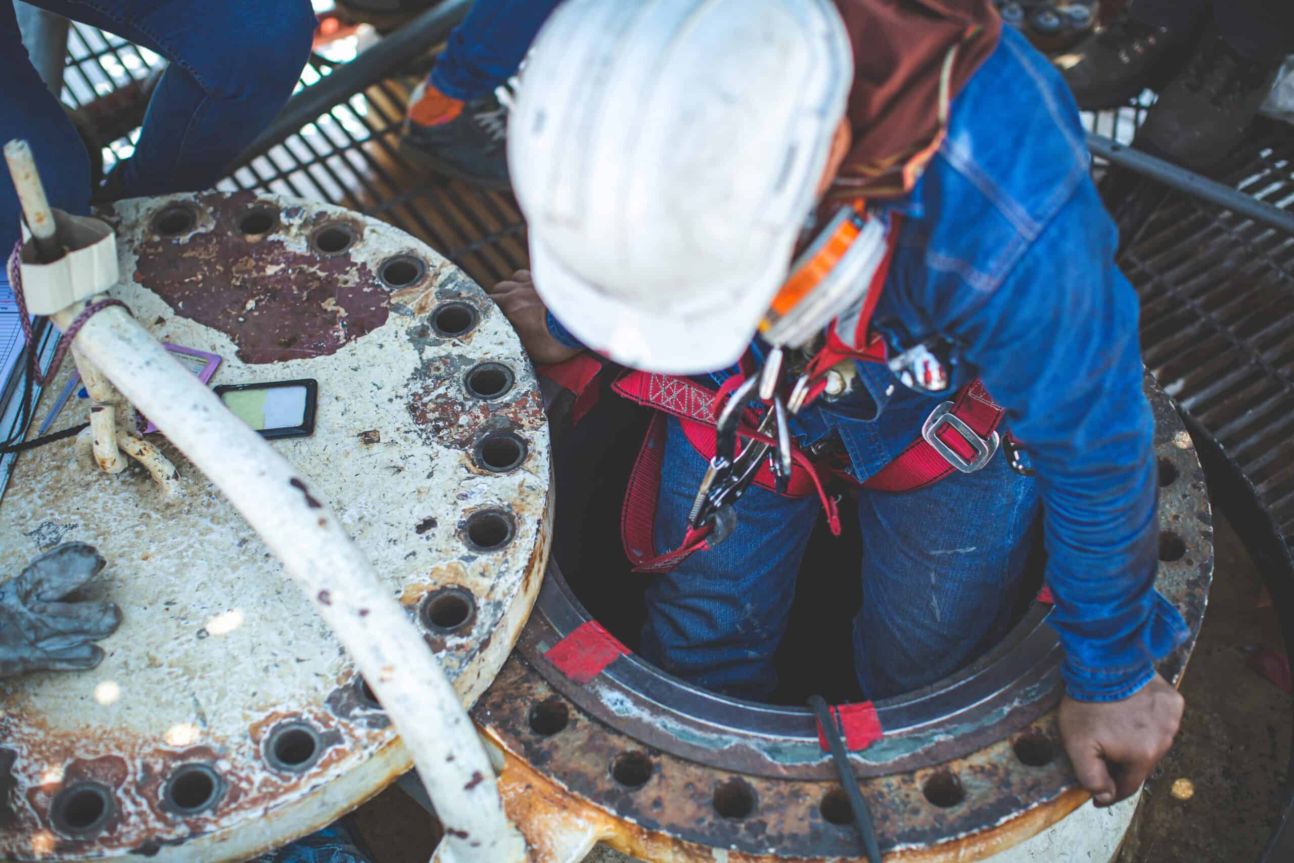 Man wearing full safety equipment, including helmet and harness, entering a confined space during confined spaces training.