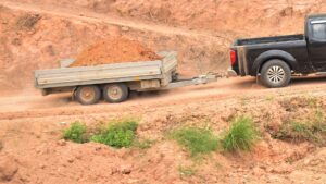 A black Nissan Navara is towing a trailer loaded with dirt on a dirt road.