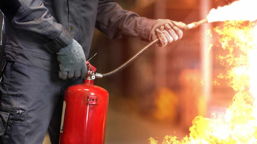 A person is using a red fire extinguisher to put out a fire with large flames.