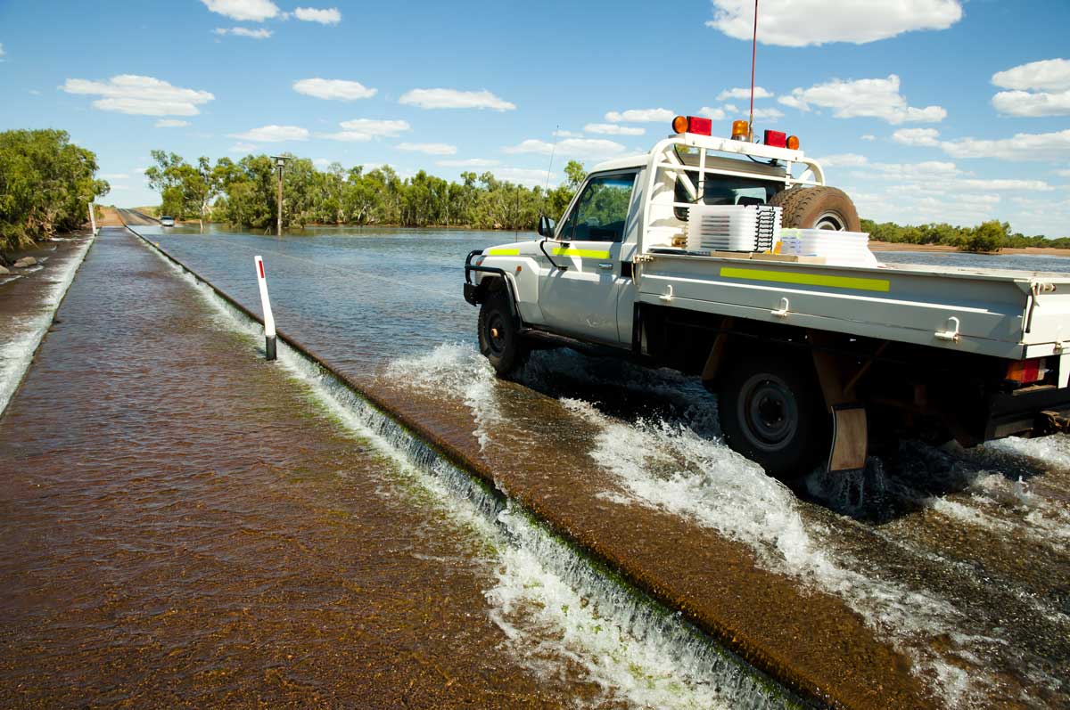 Work ute fitted with safety equipment crossing a flooded causeway in wet conditions